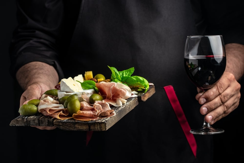 Server holding charcuterie board and glass of wine. Enjoy at Prost, one of the best places to eat in Bay City.